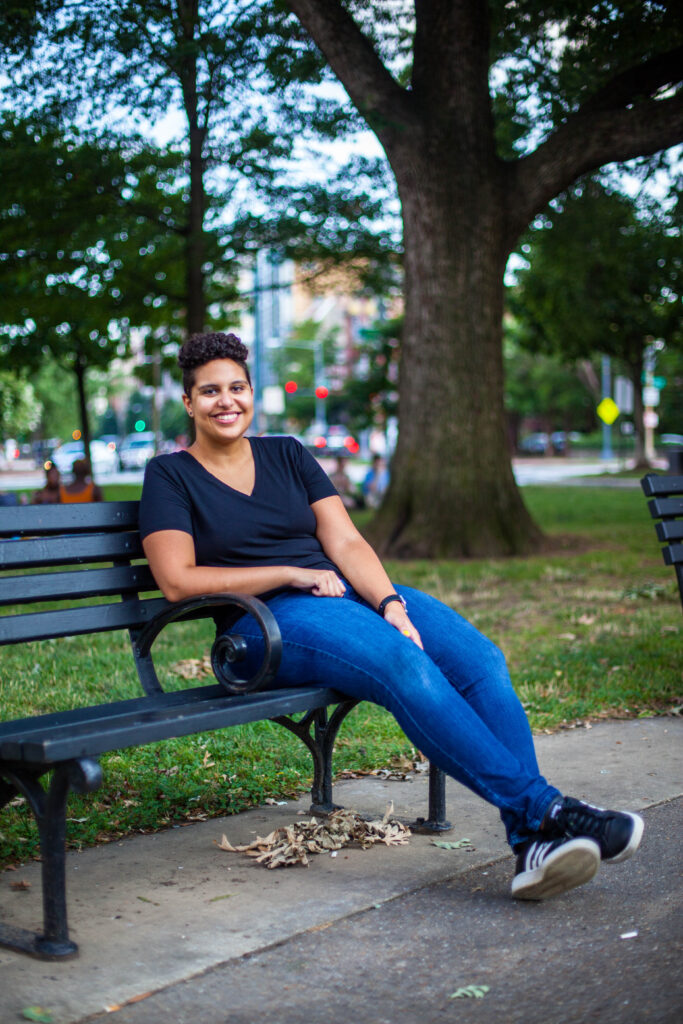 Rehana wearing a black shirt and jeans sitting on a bench in Logan Circle. She is smiling at the camera.